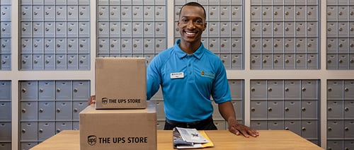 The UPS Store Associate in front of mailboxes with mail on a table.